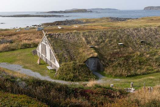 Turf-roofed dwelling with wooden frame entrance on coastal hillside overlooking bay.