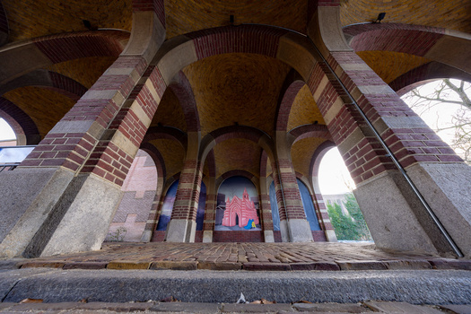 Symmetrical view through red brick arches of a covered passageway with ornate vaulted ceilings.