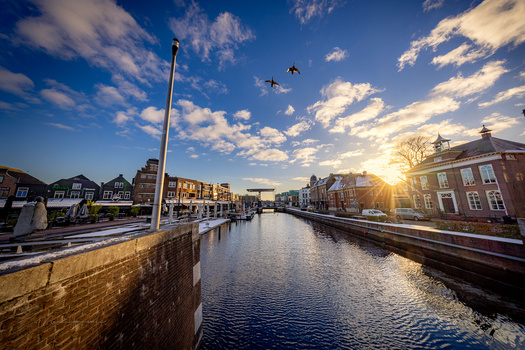 Canal with brick buildings at golden hour, birds flying overhead, clear blue sky with clouds.