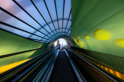 Perspective view down a modern transit tunnel with converging lines, blue ceiling, green walls, and yellow safety markings.