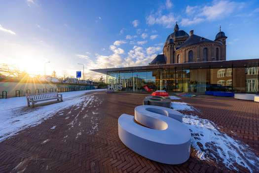 Modern white sculptural seating installations on a brick plaza at golden hour, with a historic domed building and contemporary glass structure in the background.