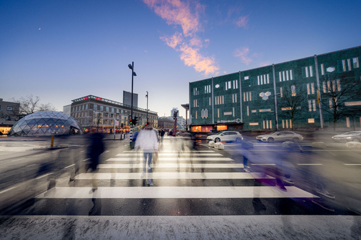 Pedestrians crossing a zebra crossing with motion blur, framed by historic European architecture and evening sky.