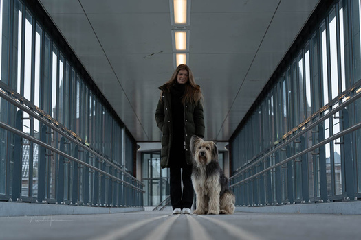 Woman walking with large shaggy dog down a symmetrical modern corridor with metal railings and bright ceiling lights.