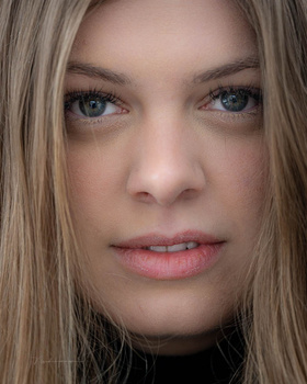 Close-up portrait of a woman with long blonde hair and blue eyes looking directly at camera.