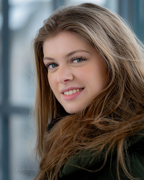 Young woman with long brown hair smiling at camera against blurred background.