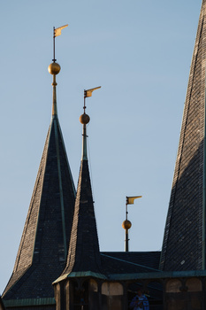 Gothic architecture with multiple spires topped by golden weathervanes against clear blue sky.