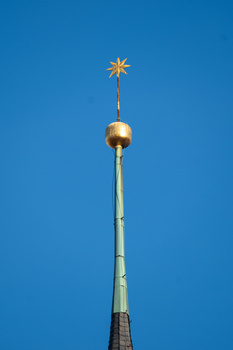 Golden orb and star spire atop a tapered church tower against clear blue sky.