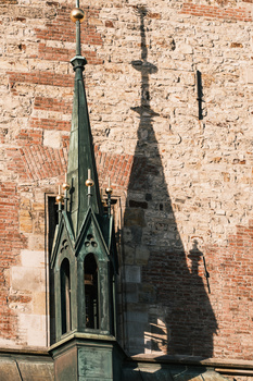 Gothic church spires with ornate stonework casting shadows against a brick wall.