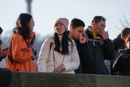Four people standing outdoors wearing winter clothing, smiling and engaged in conversation.