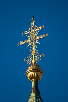 Golden ornamental cross atop a dome finial against a clear blue sky.