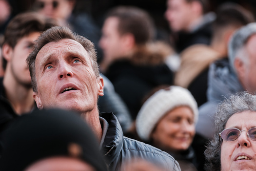 Man in black jacket looking upward among a crowd of spectators at an outdoor event.