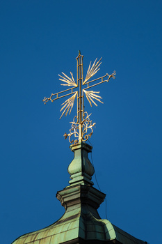 Ornate golden cross atop a green copper dome against clear blue sky.