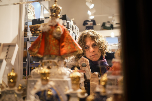 Woman examining small golden figurines and objects displayed in a museum case with warm gallery lighting.