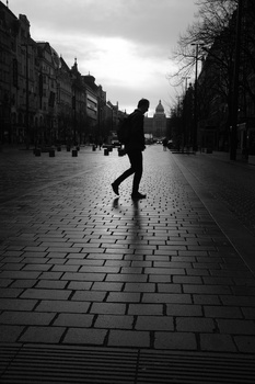 Silhouetted figure running down a wet, empty urban street lined with buildings.