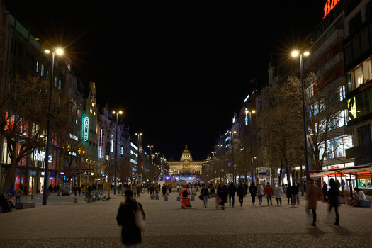 Nighttime street scene with crowds of pedestrians walking toward an illuminated building in the distance.