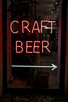 Neon sign reading 'CRAFT BEER' with a directional arrow, displayed in a dark storefront window.