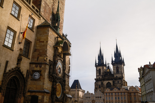 Historic Prague square with ornate medieval buildings and twin Gothic spires in the background.