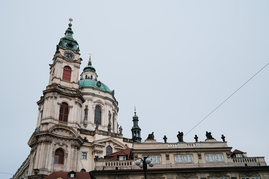 Ornate church tower with cream and green facade, crosses adorning roofline, against overcast sky.