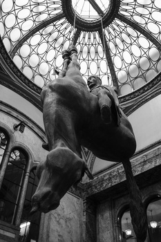 Upward view of a classical male sculpture beneath an ornate domed ceiling with geometric patterns.