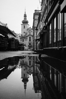 European street with church tower reflected in wet pavement puddle.
