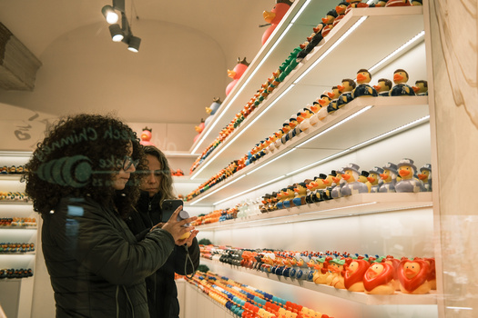 Videographer filming illuminated shelves stocked with colorful produce in a retail display.