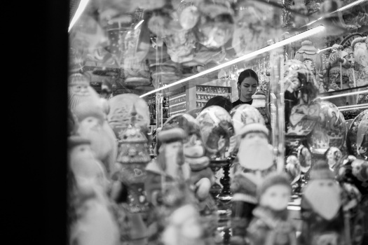 Woman examining merchandise displayed in storefront window with reflective glass and multiple items visible.