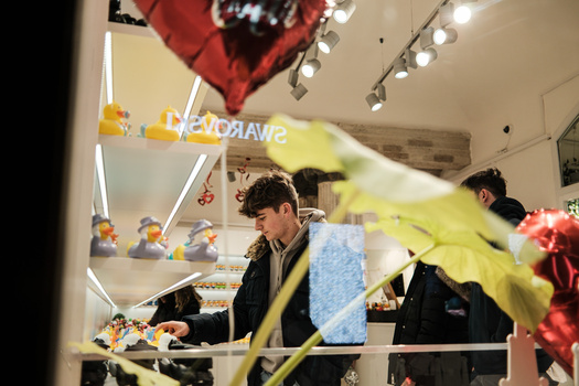 Customer service counter with staff member assisting shopper, flowers in foreground, warm interior lighting.