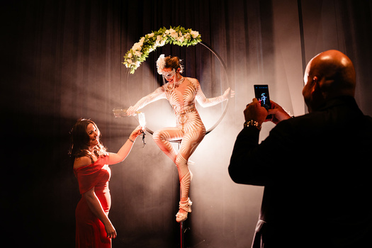 Performer suspended in air wearing gold bodysuit and floral headpiece during theatrical production shoot.
