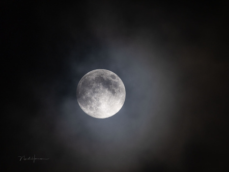 Full moon surrounded by dark clouds against a black night sky.