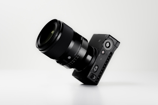 Black mirrorless camera body with attached black telephoto lens on white surface.