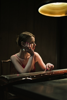 Musician performing at a keyboard under warm overhead lighting against a dark background.