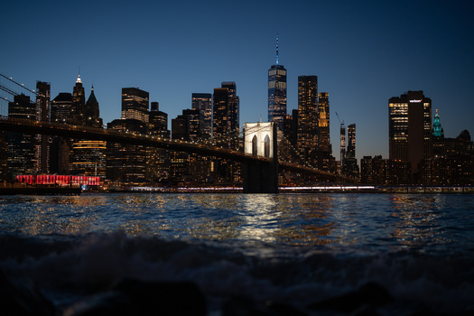 Manhattan skyline at twilight with illuminated skyscrapers reflected in dark water below.