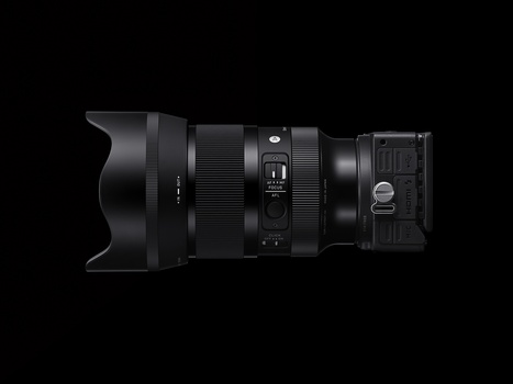 Side view of a professional zoom lens with hood, focus ring, and lens mount visible against black background.