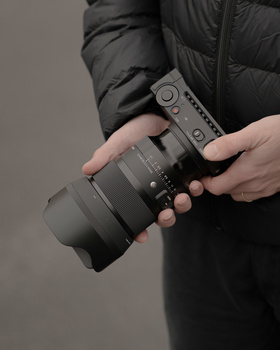 Photographer holding a telephoto lens while wearing a black puffer jacket.