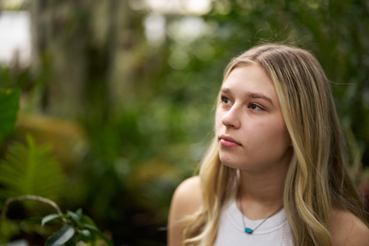 Blonde woman with long hair gazing away in a garden setting with soft natural light.