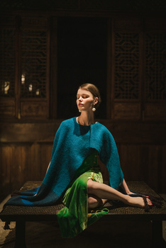 Woman in blue draped fabric seated on a bench against a dark stone architectural backdrop.