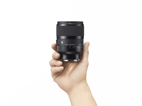 Hand holding a black telephoto lens with focus ring and distance scale markings visible.