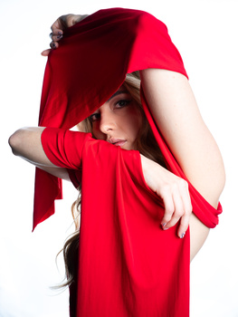 Person in bright red fabric posing with arm raised and hood covering face against white background.