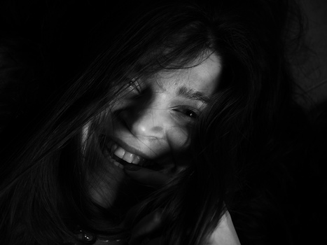 Woman with long dark hair smiling at camera against dark background in black and white portrait.