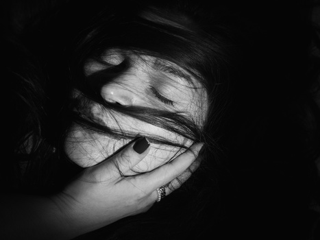 Black and white portrait of a person wearing glasses with hair partially covering their face and hand near mouth.