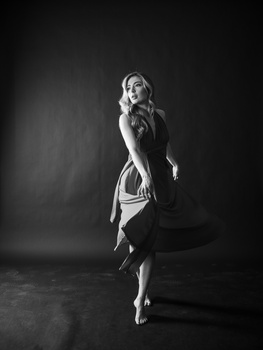 Woman in geometric patterned dress posing against dark background in black and white studio portrait.