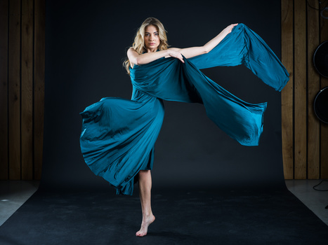 Woman in flowing blue draped fabric mid-motion against dark background.
