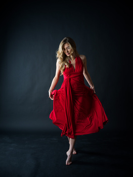 Woman in red dress against dark background, mid-motion with fabric flowing.