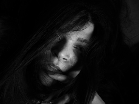 Woman with long dark hair photographed against a black background in high-contrast black and white.