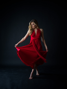 Woman in red wrap dress with flowing fabric against dark background.