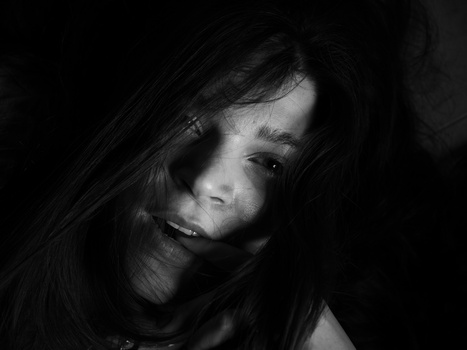 Woman with long dark hair looking downward against a black background.