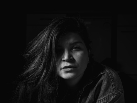Woman with long dark hair in dramatic low-key portrait lighting against black background.