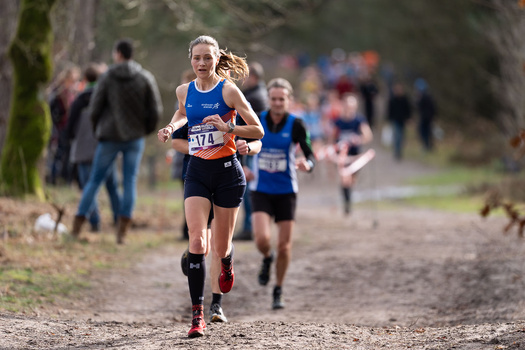 Female runner wearing bib number 447 leads the race on a dirt path with spectators blurred in the background.