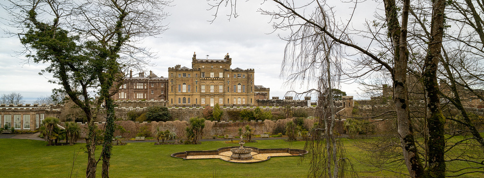 Stone castle on hilltop viewed across manicured grounds framed by bare winter trees.