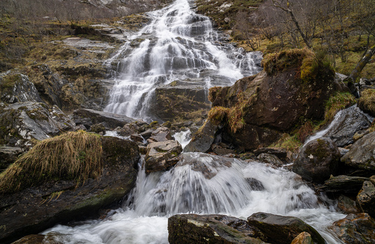 Multi-tiered waterfall cascading over moss-covered rocks in a forested stream.